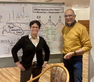 Das Foto zeigt Marja Költzsch und Heinz Pilart vor einer Schautafel für den Workshop im November 2025